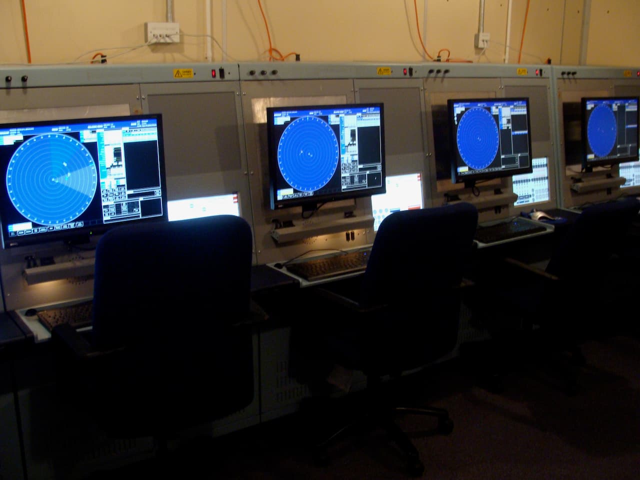 A row of Airwaves training stations, each with a blue radar display, supporting screen, keyboard and chair.